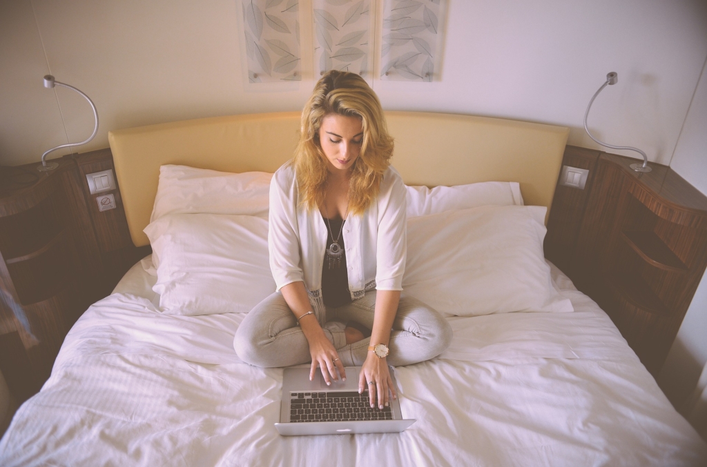 Uma mulher loira com o notebook na cama digitando.