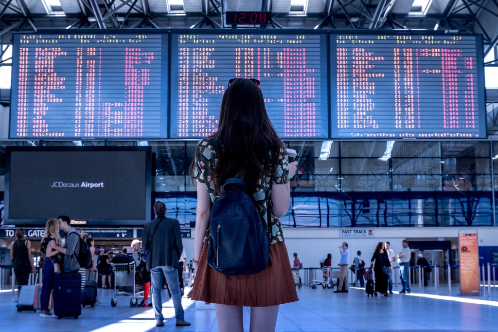 Uma mulher de costas olhando para um painel gigante do aeroporto decidindo para onde quer ir.